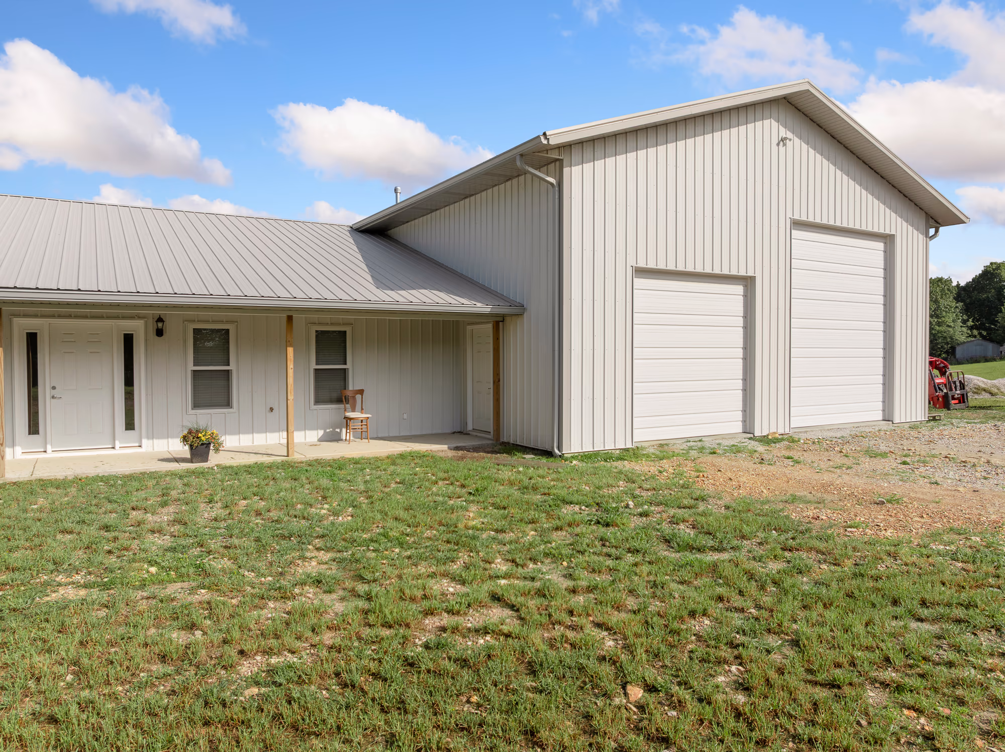 A light tan metal barndominium with an attached two-bay shop and a covered porch running along the living wing