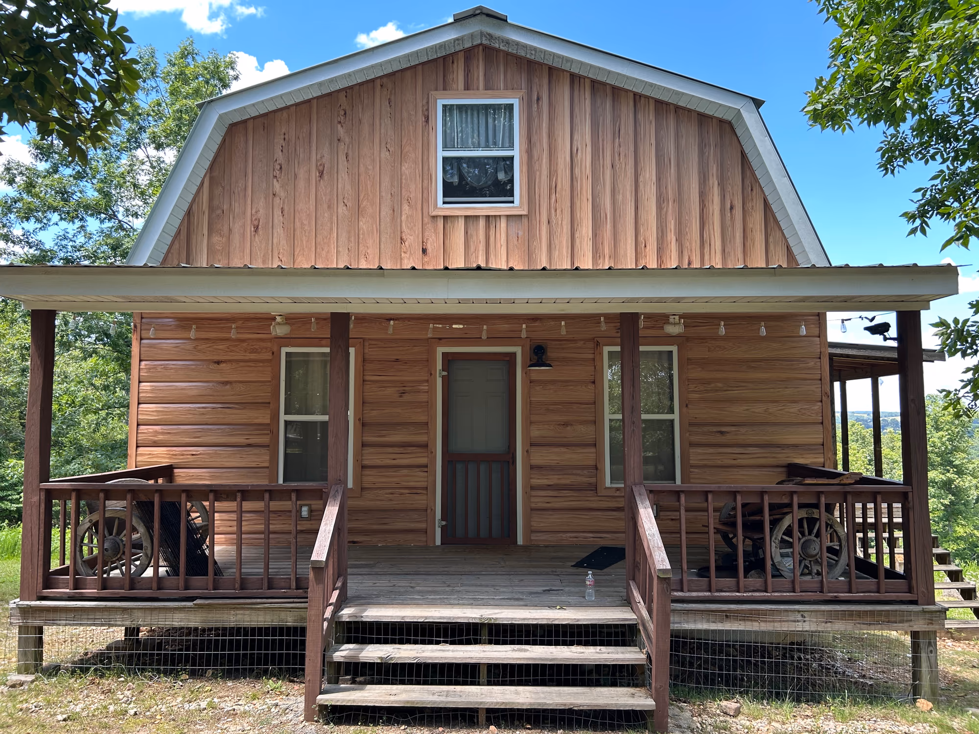 A gambrel-roofed cabin clad in TrueLog metal siding that reproduces the look of stacked logs, with a covered front porch